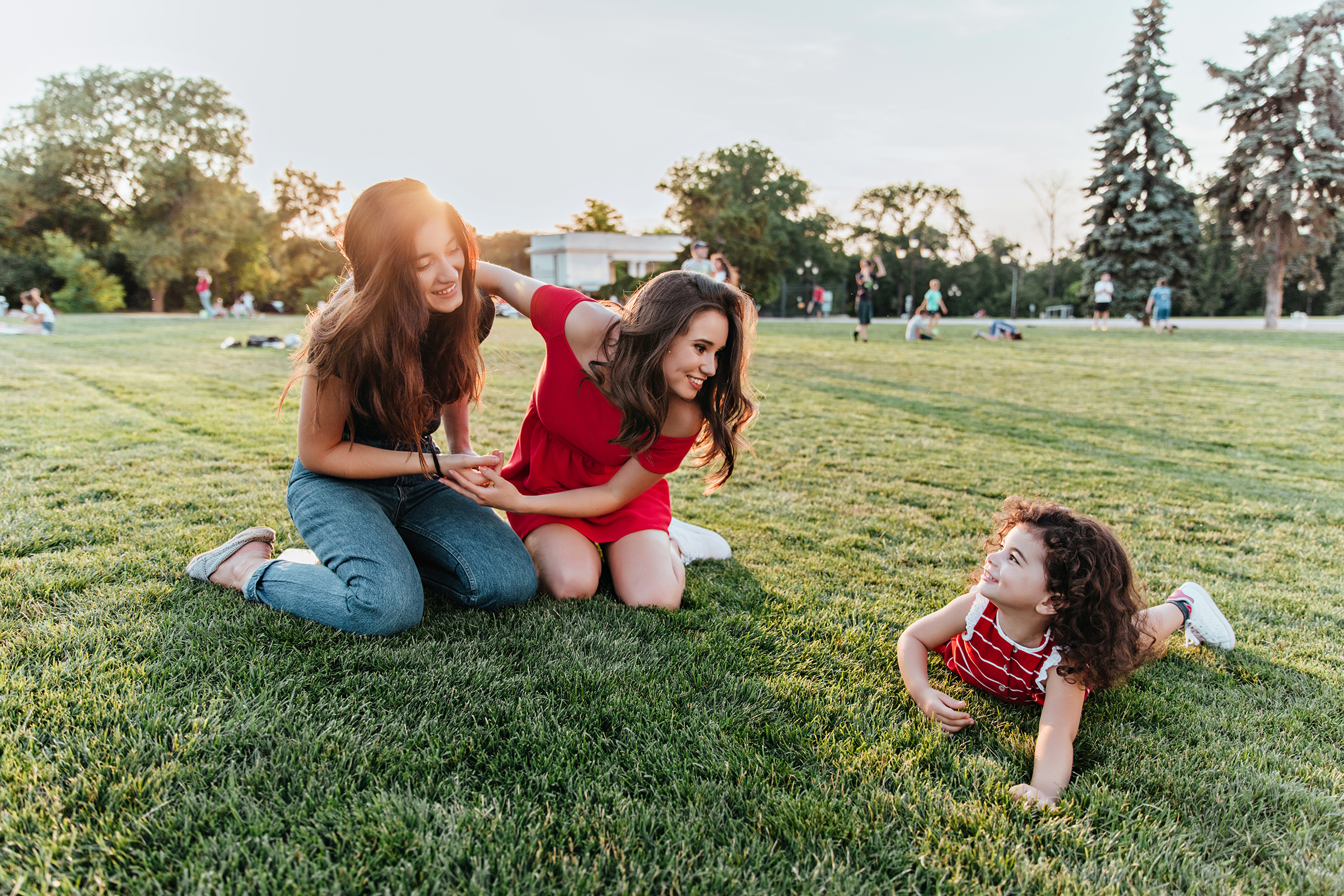 Attractive female friends posing on the grass with little kid. P